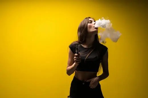 attractive woman standing vaping yellow wall