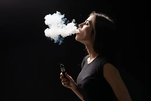 young beautiful brunette woman smoking vaping e cigarette with smoke black wall