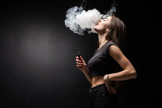 young sexy woman is vaping smoking e cigarette cloud vapor black wall